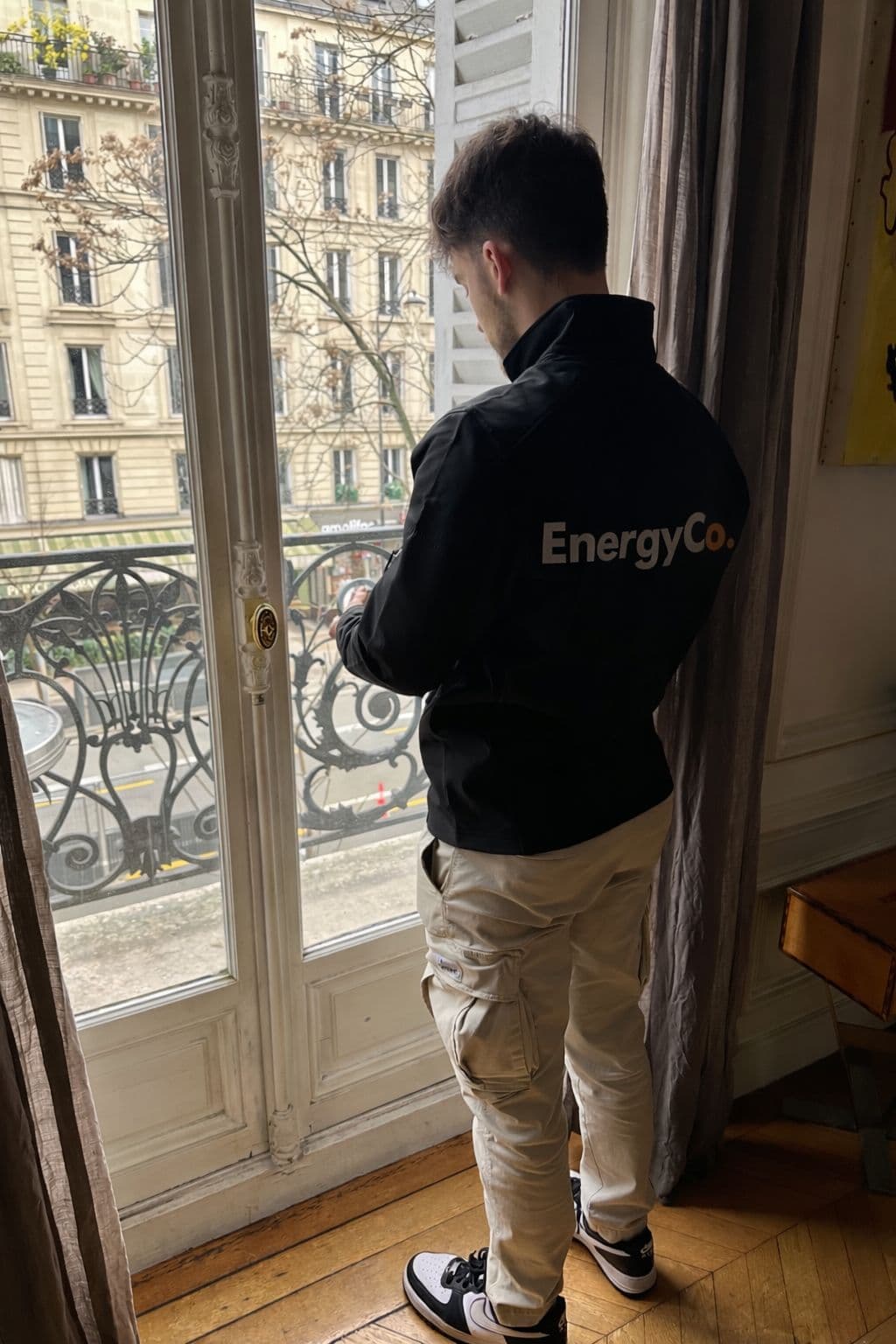 Technicien EnergyCo réalisant une mesure à une fenêtre haussmannienne à Paris